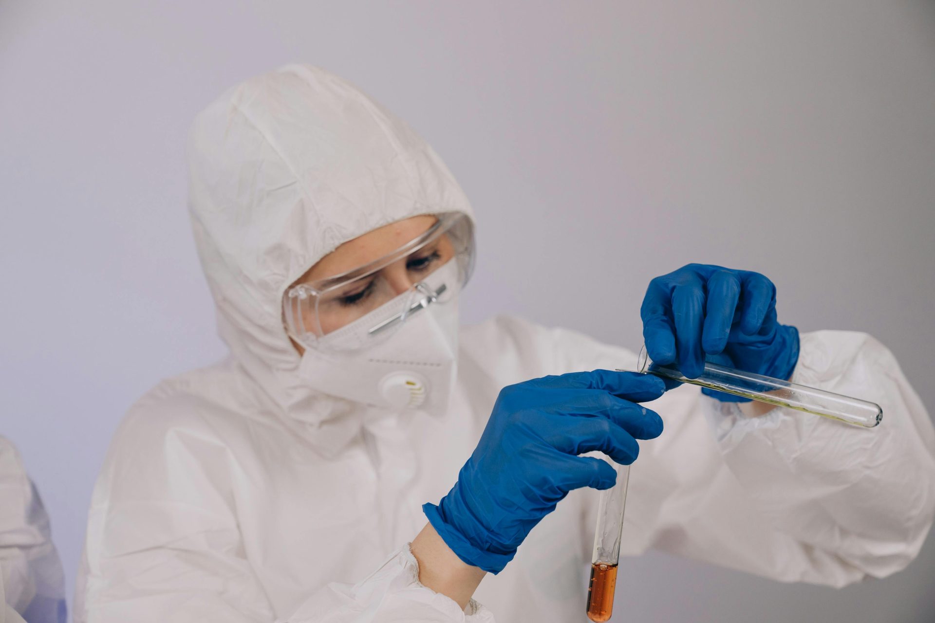 Person in White Protective Suit Wearing Blue Gloves Holding Glass Test Tubes. Medical Marijuana and Work Drug Tests